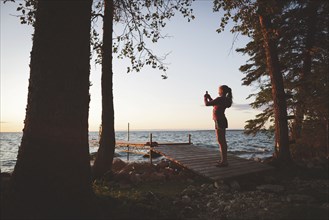 Caucasian girl photographing sunset and lake