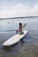 Caucasian girl rowing on paddleboard in lake