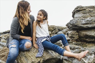 Hispanic mother and daughter sitting at tide pools