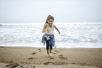 Hispanic girl walking barefoot on beach