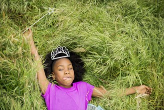 Black girl in princess tiara laying in grass