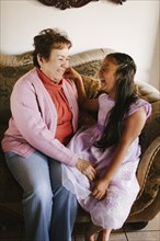 Hispanic grandmother and granddaughter laughing on sofa