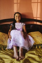 Hispanic girl wearing party dress on bed