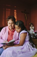 Hispanic grandmother and granddaughter ready book on bed
