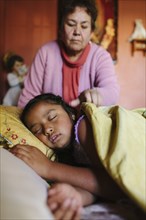 Hispanic grandmother tucking granddaughter into bed