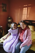 Hispanic grandmother and granddaughter sitting on bed