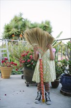 Girl hiding face on patio with broom