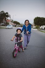 Grandmother teaching granddaughter to ride bicycle on suburban street