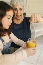 Grandmother pouring juice for granddaughter in kitchen