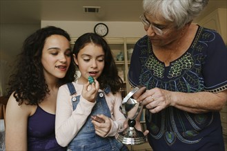 Grandmother helping granddaughters apply lipstick in mirror