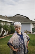 Older woman standing with hands on hips in backyard