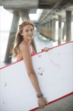 Woman carrying surfboard under boardwalk on beach