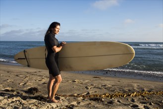 Hispanic surfer carrying surfboard on beach