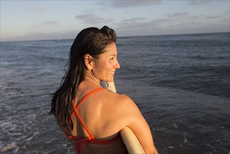 Hispanic woman holding surfboard in ocean