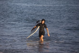 Hispanic surfer carrying surfboard in ocean