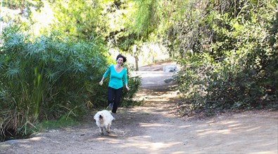 Caucasian woman running with dog on dirt path