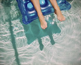 Feet of Caucasian woman floating on raft in swimming pool