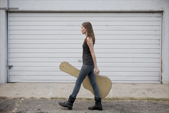 Caucasian woman carrying guitar case on sidewalk