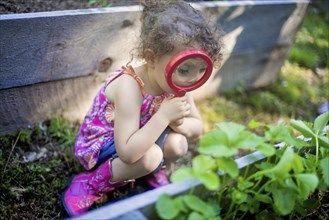 Girl examining garden plants with magnifying glass
