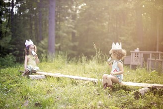 Girls playing telephone on wooden log in garden