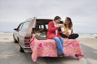 Caucasian mother and daughter eating picnic in car trunk on beach
