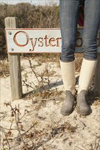 Woman wearing boots near sign on beach