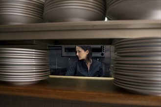 Working chef viewed through stacks of plates in restaurant kitchen