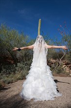 Bride standing with arms outstretched in desert near cactus