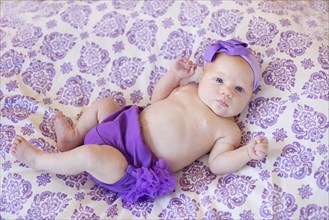 Baby girl wearing purple diaper and headband on blanket