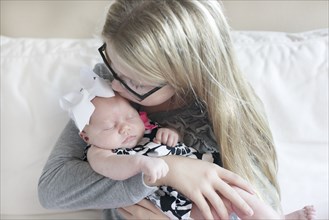 Caucasian girl kissing newborn sister on sofa