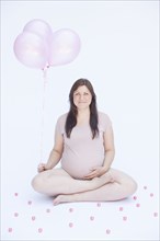 Pregnant Caucasian woman holding bunch of balloons