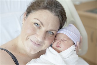 Caucasian mother holding newborn daughter in hospital bed