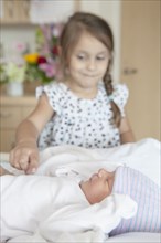 Girl admiring newborn sister on hospital bed