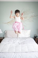 Hispanic girl jumping on bed