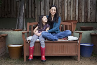 Mother and daughter sitting on bench in backyard
