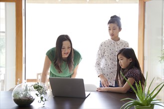 Mother and daughters using laptop in dining room