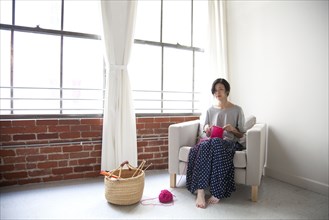 Taiwanese woman knitting in armchair near window