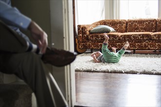 Businessman tying shoes as son plays in livingroom