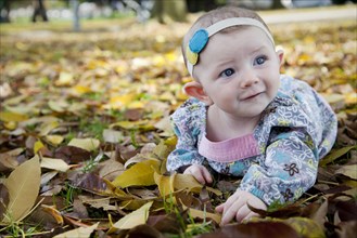 Mixed race baby girl crawling in autumn leaves