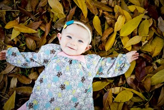 Mixed race baby girl laying in autumn leaves