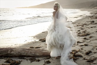 Caucasian bride walking on beach