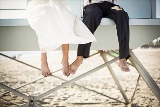 Asian bride and groom sitting on lifeguard hut on beach