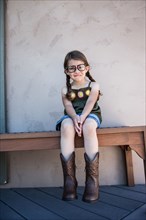 Caucasian girl wearing eyeglasses and cowboy boots on bench