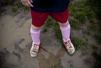 Girl wearing sneakers in mud puddle