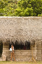 Woman standing under thatched hut roof