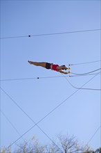Acrobat hanging from trapeze under blue sky