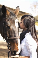 Teenage girl kissing horse in stable