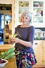 Older Caucasian woman shucking corn in kitchen