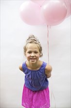 Smiling girl wearing tiara holding pink balloons