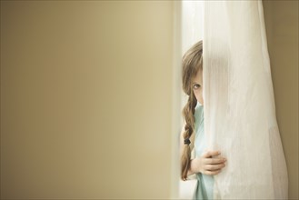 Shy Caucasian girl peeking around curtain